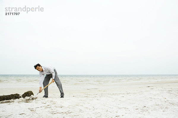 Mann am Strand  sich bücken und im Sand graben  lächelnd in die Kamera schauen