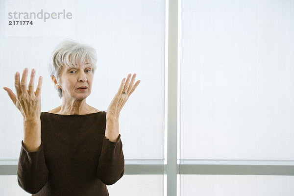 Seniorin mit erhobenen Händen und Blick auf die Kamera