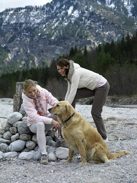 Zwei junge Frauen mit Hund am Flussufer