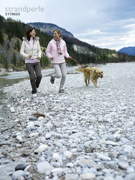 Zwei junge Frauen Joggen mit Hund am Flussufer