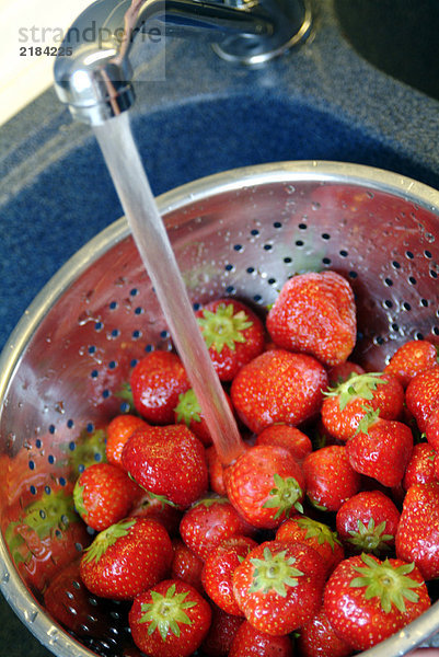 Nahaufnahme von Erdbeeren in Sieb unter Wasserhahn