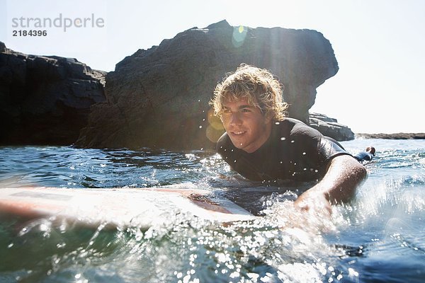 Mann auf dem Surfbrett im Wasser liegend.