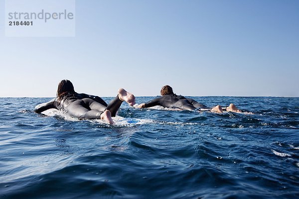 Ein Paar geht auf Surfbrettern ins Wasser.