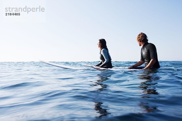 Ein Paar sitzt auf Surfbrettern im Wasser.