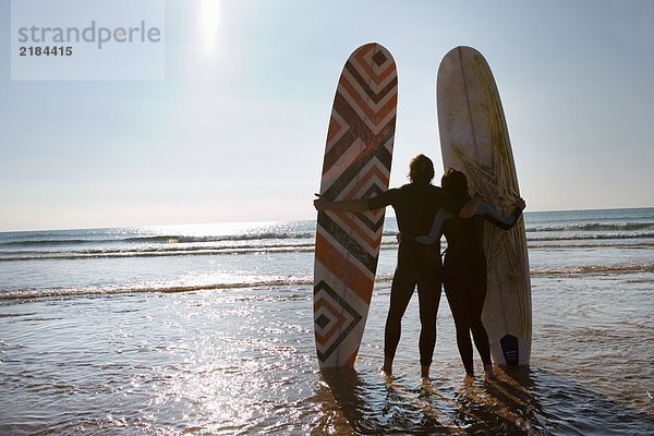 Paar mit Surfbrettern am Strand.