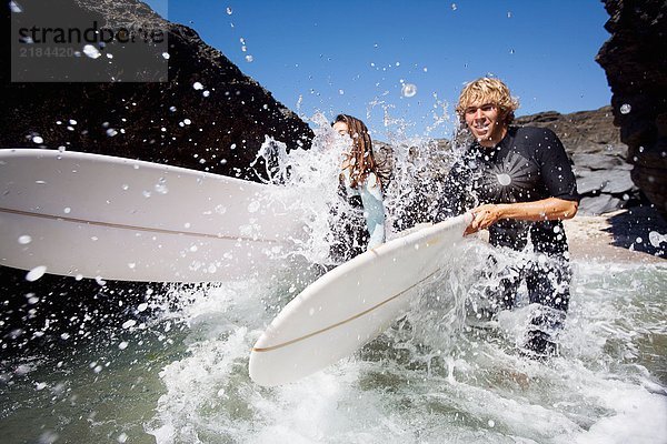 Ein Paar läuft im Wasser mit lächelnden Surfbrettern.