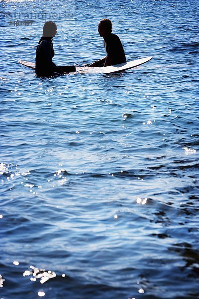 Paar auf Surfbrettern im Wasser lächelnd.