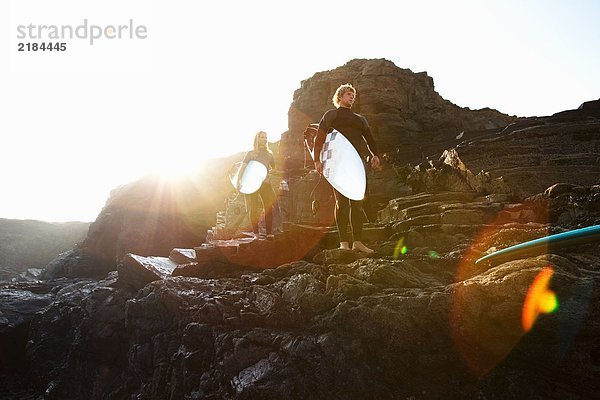 Paar auf großen Felsen stehend mit Surfbrettern.