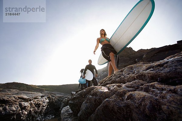 Drei Leute mit Surfbrettern auf großen Felsen lächelnd.