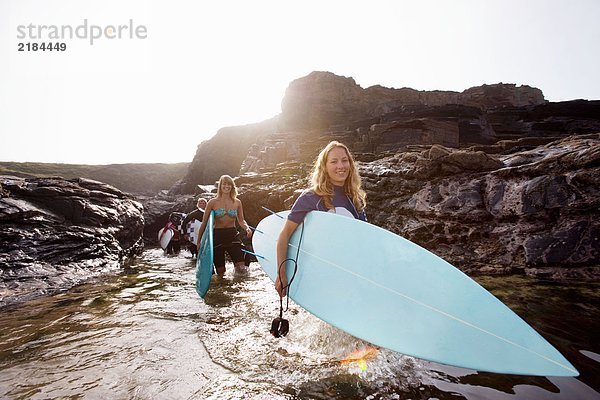 Vier Leute mit Surfbrettern im Wasser lächelnd.