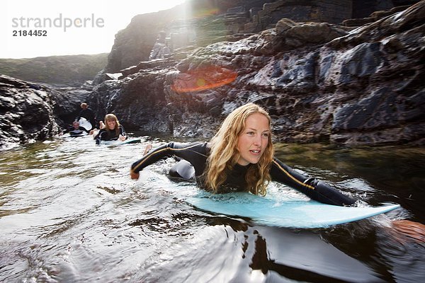 Vier Leute liegen auf Surfbrettern im Wasser und lächeln.