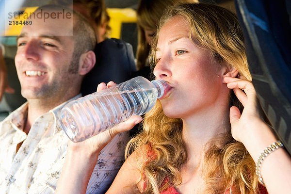 Vier Leute in einem Van lächeln mit einer Frau  die Wasser trinkt.