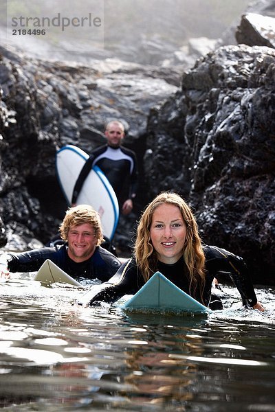 Drei Leute mit lächelnden Surfbrettern.