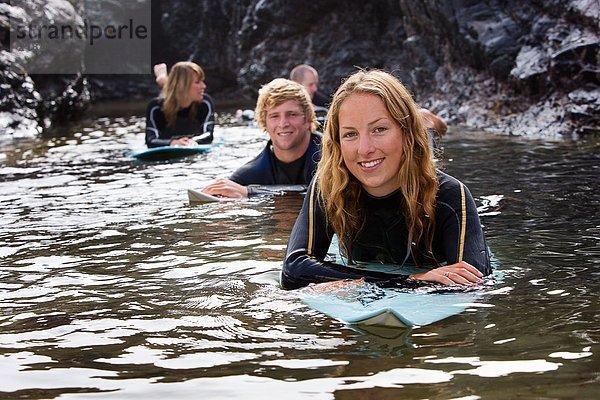 Vier Leute liegen auf Surfbrettern im Wasser und lächeln.