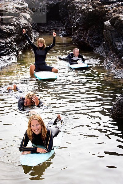 Vier Leute haben Spaß auf Surfbrettern im Wasser und lächeln.