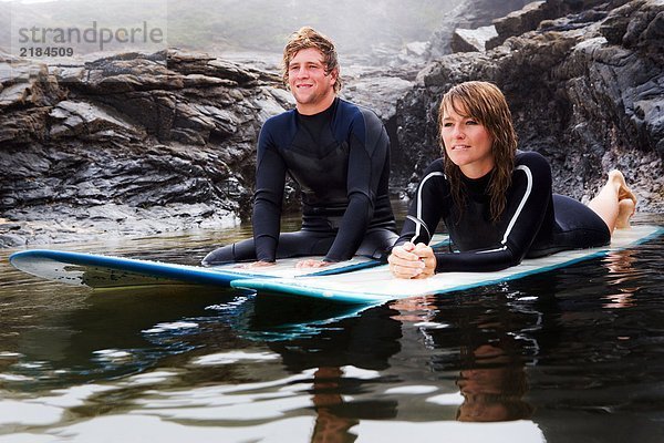 Paar auf Surfbrettern im Wasser liegend  lächelnd.