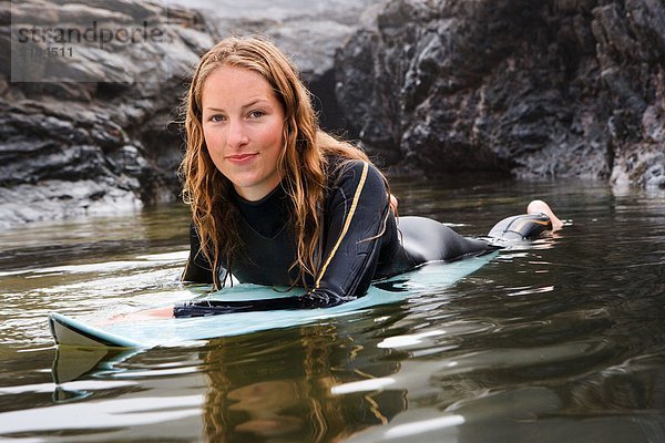Frau lächelnd auf dem Surfbrett im Wasser liegend.