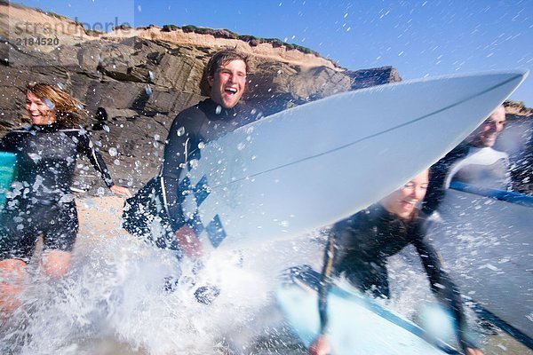 Vier Leute laufen mit lächelnden Surfbrettern ins Wasser.