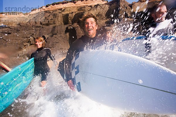 Vier Leute laufen mit lächelnden Surfbrettern ins Wasser.