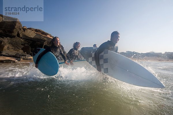 Vier Leute laufen mit lächelnden Surfbrettern ins Wasser.