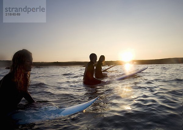 Vier Leute sitzen auf Surfbrettern im Wasser und lächeln.