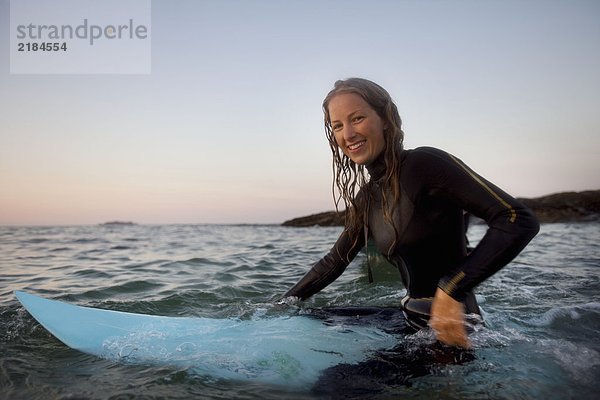 Frau sitzt auf dem Surfbrett im Wasser und lächelt.