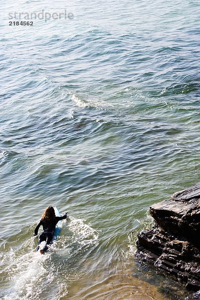 Frau liegt auf dem Surfbrett im Wasser.