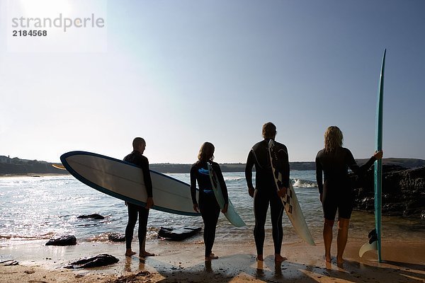 Vier Leute mit Surfbrettern am Strand.