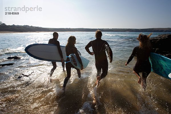 Vier Leute laufen mit Surfbrettern ins Wasser.