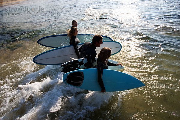 Vier Leute  die Surfbretter ins Wasser tragen  lachend.