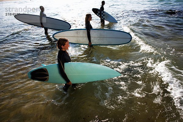 Vier Leute stehen mit Surfbrettern im Wasser und lächeln.