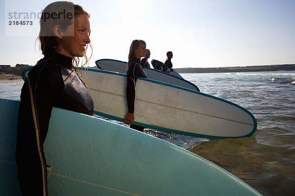 Vier Leute stehen mit Surfbrettern im Wasser und lächeln.