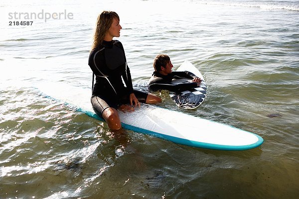 Ein Paar schwebt auf Surfbrettern im Wasser und lächelt.