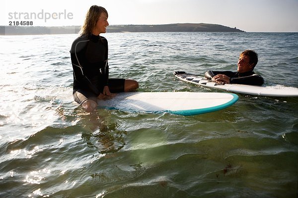 Ein Paar schwebt auf Surfbrettern im Wasser und lächelt.