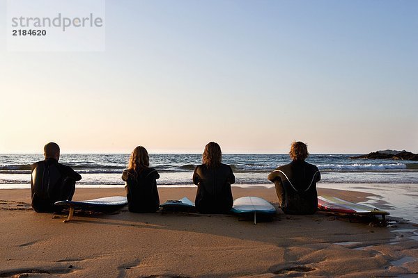 Vier Leute sitzen am Strand mit Surfbrettern.