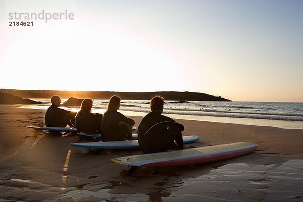 Vier Leute sitzen am Strand mit Surfbrettern.