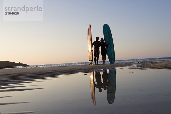 Paar am Strand stehend mit Surfbrettern.