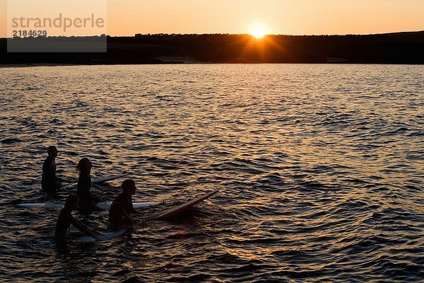 Vier Leute sitzen auf Surfbrettern im Wasser.