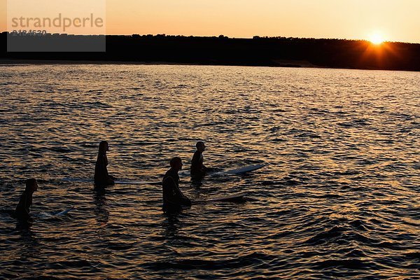 Vier Leute sitzen auf Surfbrettern im Wasser.