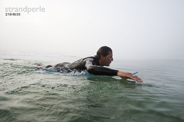 Mann auf dem Surfbrett im Wasser liegend.