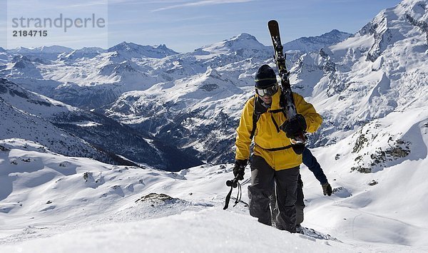 Zwei männliche Skifahrer  die mit Skiern den Bergrücken hinaufgehen.