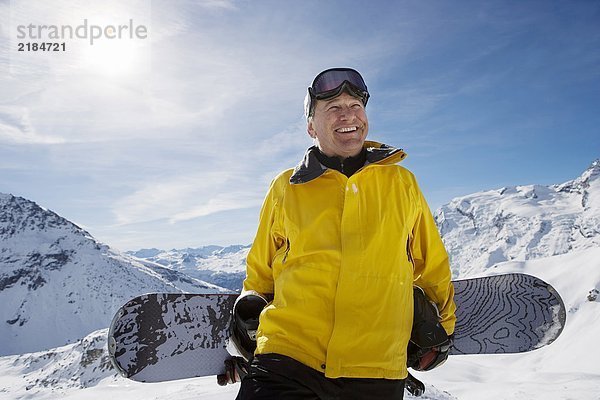Erwachsener Snowboarder mit Snowboard am Berg  Portrait