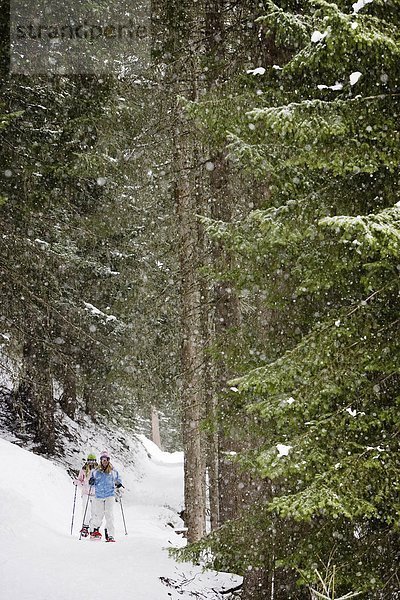 Zwei junge blonde Frauen stehen im Wald in Schneeschuhen  Portrait