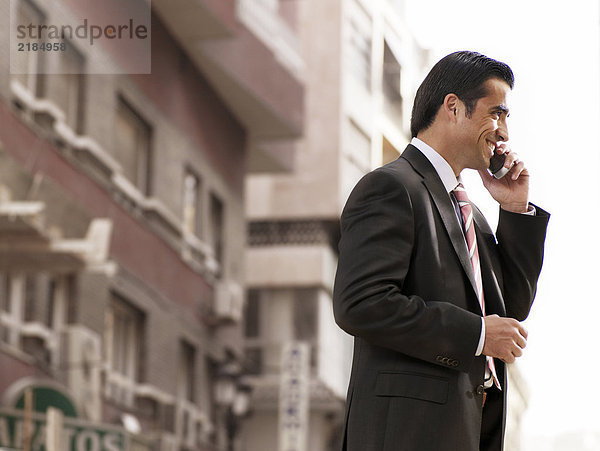 Junger Geschäftsmann auf der Straße stehend mit dem Handy  lächelnd
