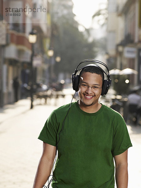 Junger Mann mit Kopfhörer auf der Straße stehend  lächelnd  Portrait