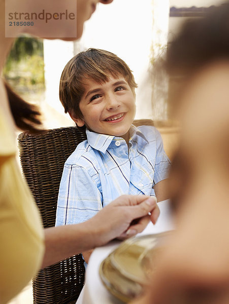 Junge (4-6) am Tisch sitzend mit Familie im Garten  lächelnd