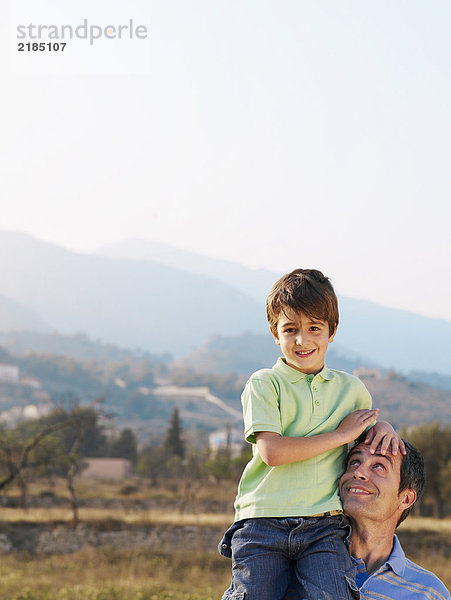 Vater mit Sohn (4-6) auf der Schulter  lächelnd