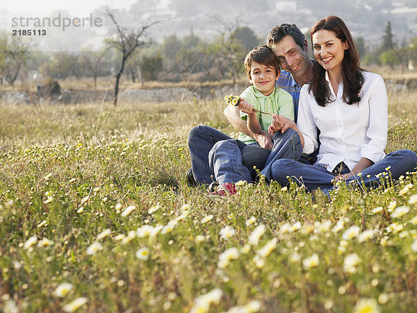 Eltern und Sohn (6-8) im Feld sitzend  lächelnd  Porträt