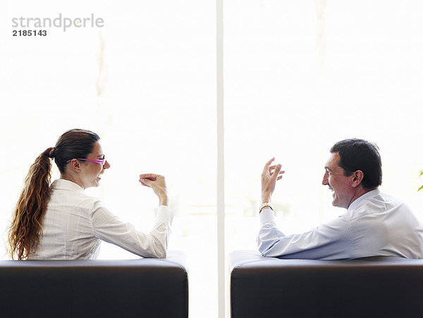 Geschäftsmann und Frau in Sesseln sitzend  redend  Rückansicht