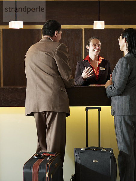 Hotelrezeptionistin im Gespräch mit Geschäftsmann und Frau  lächelnd
